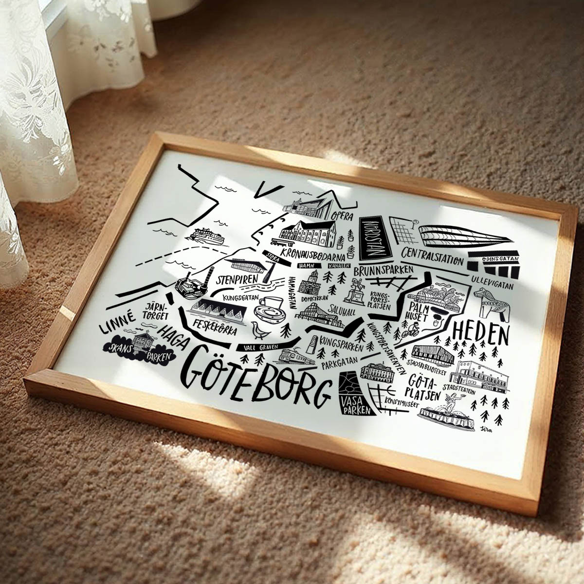 Framed map of Gothenburg with black illustrations on a white background, placed on a textured surface.