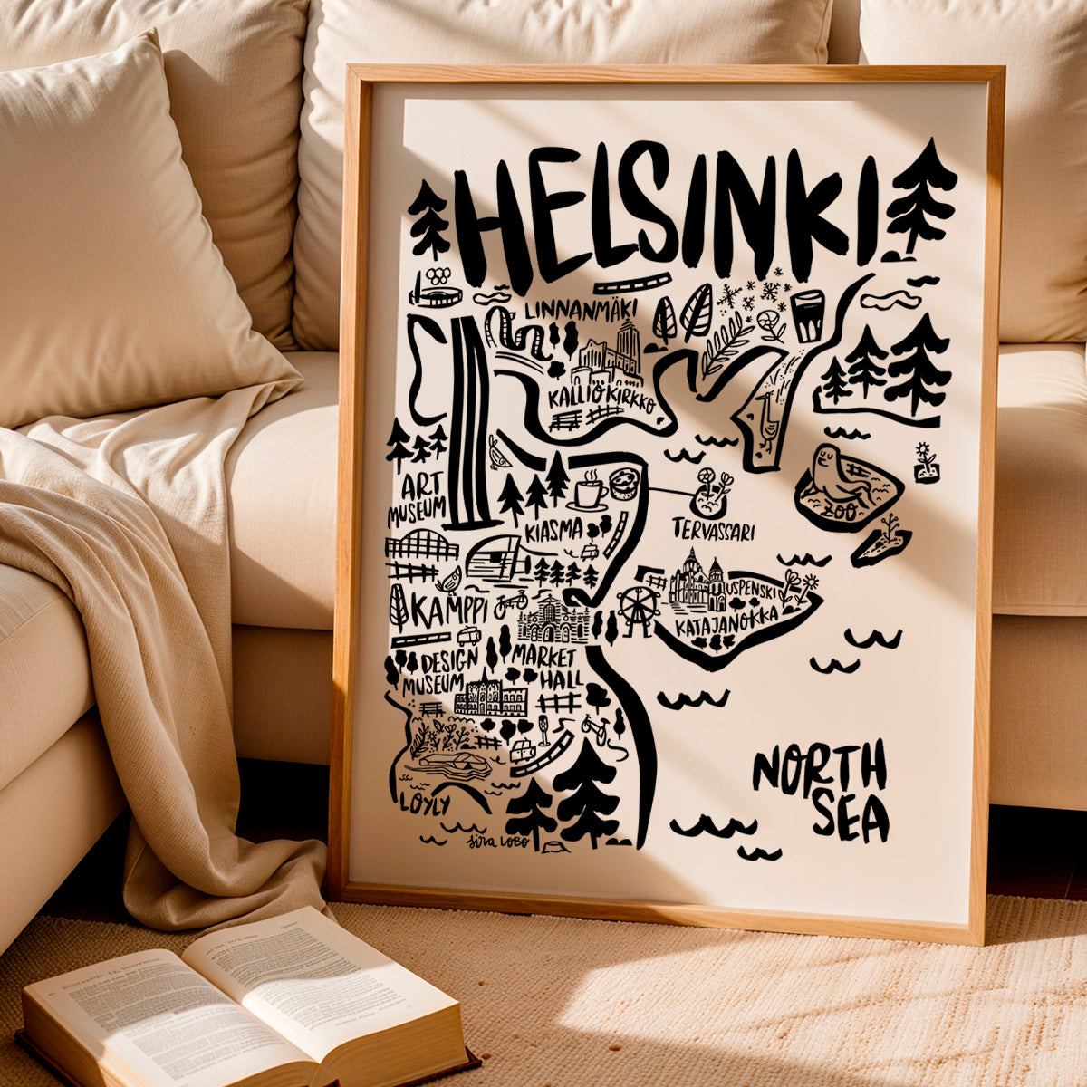 Framed map of Helsinki on a beige couch with an open book.