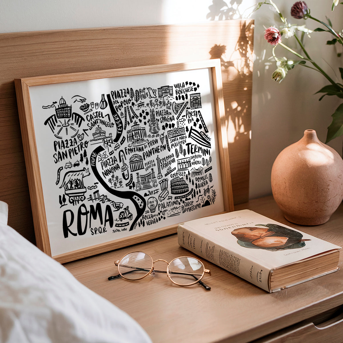 Framed map of Rome on a wooden surface with a book and glasses.