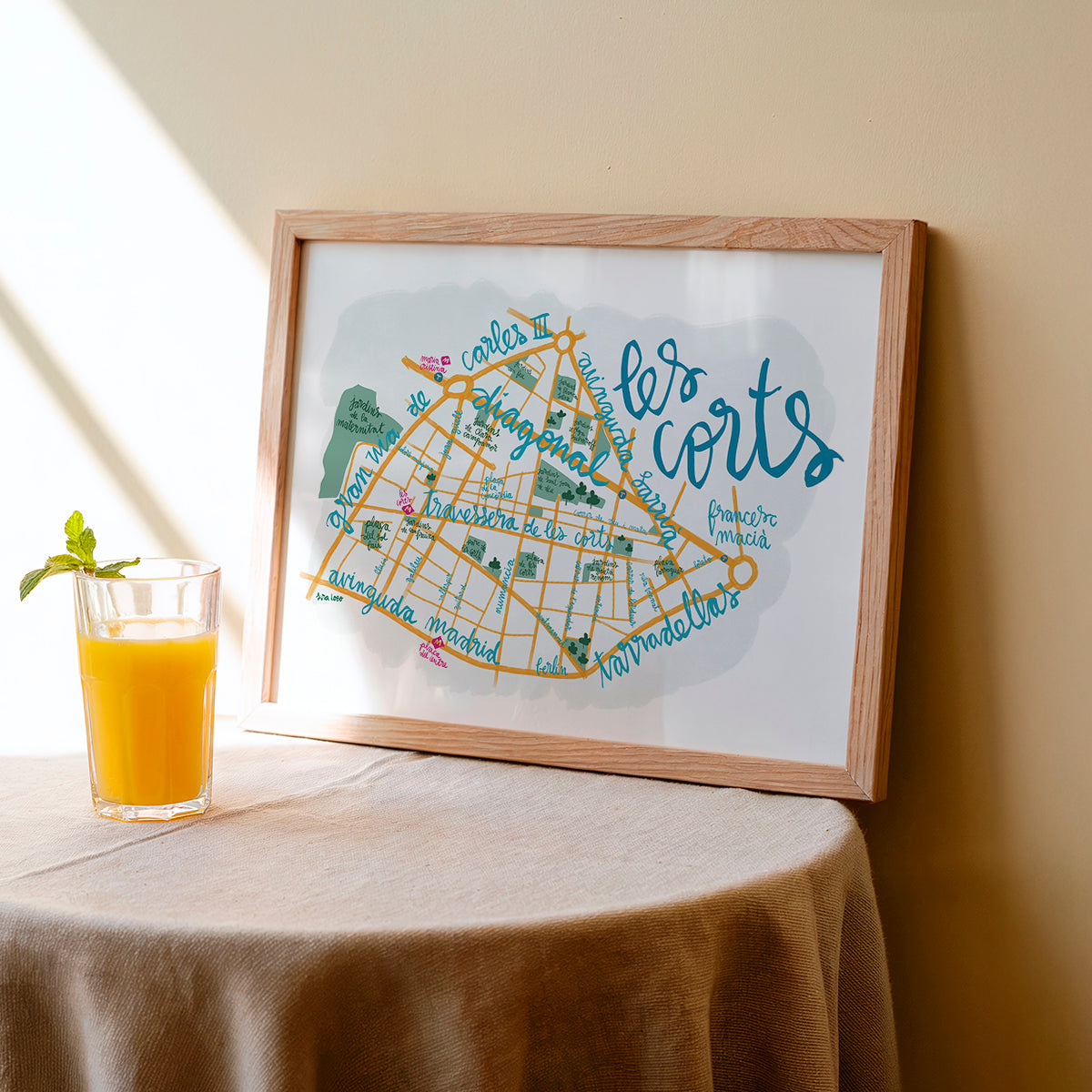Framed map of 'les corts' on a table with a glass of orange juice.
