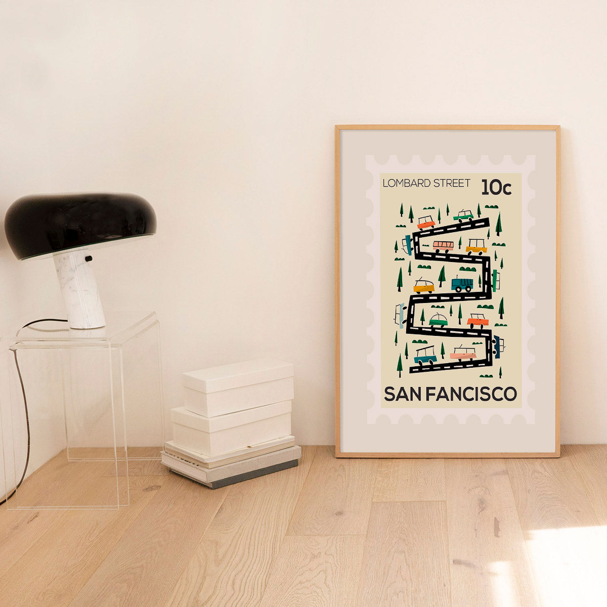 Framed poster of Lombard Street in San Francisco on a wall in a room with a lamp and books.