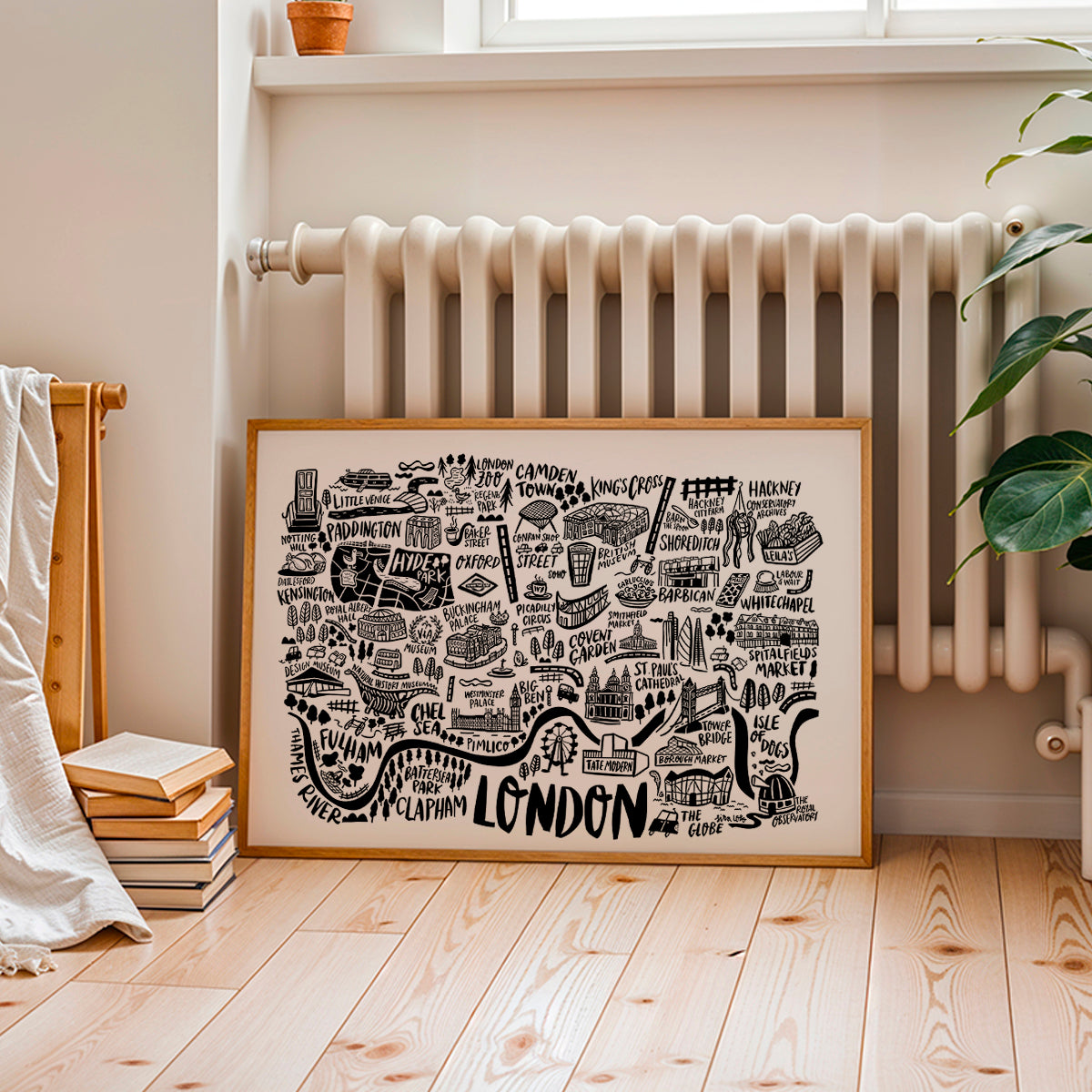 Framed map of London on a wall above a radiator in a room with books and a plant.