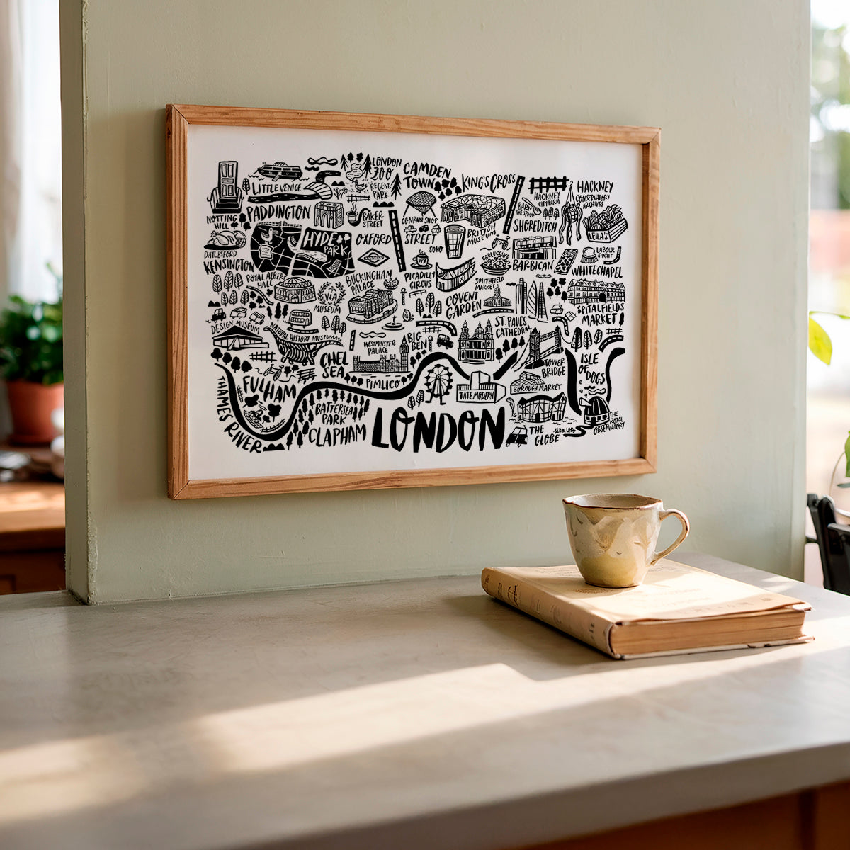 Framed map of London on a wall above a table with a book and mug.
