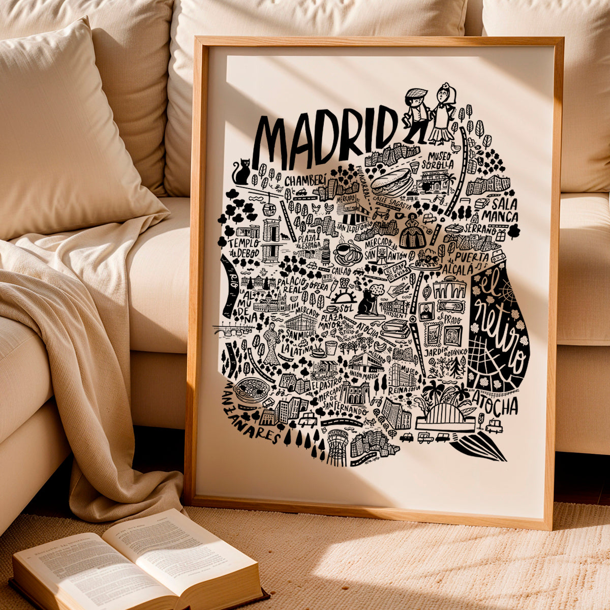 Framed map of Madrid on a beige couch with an open book.