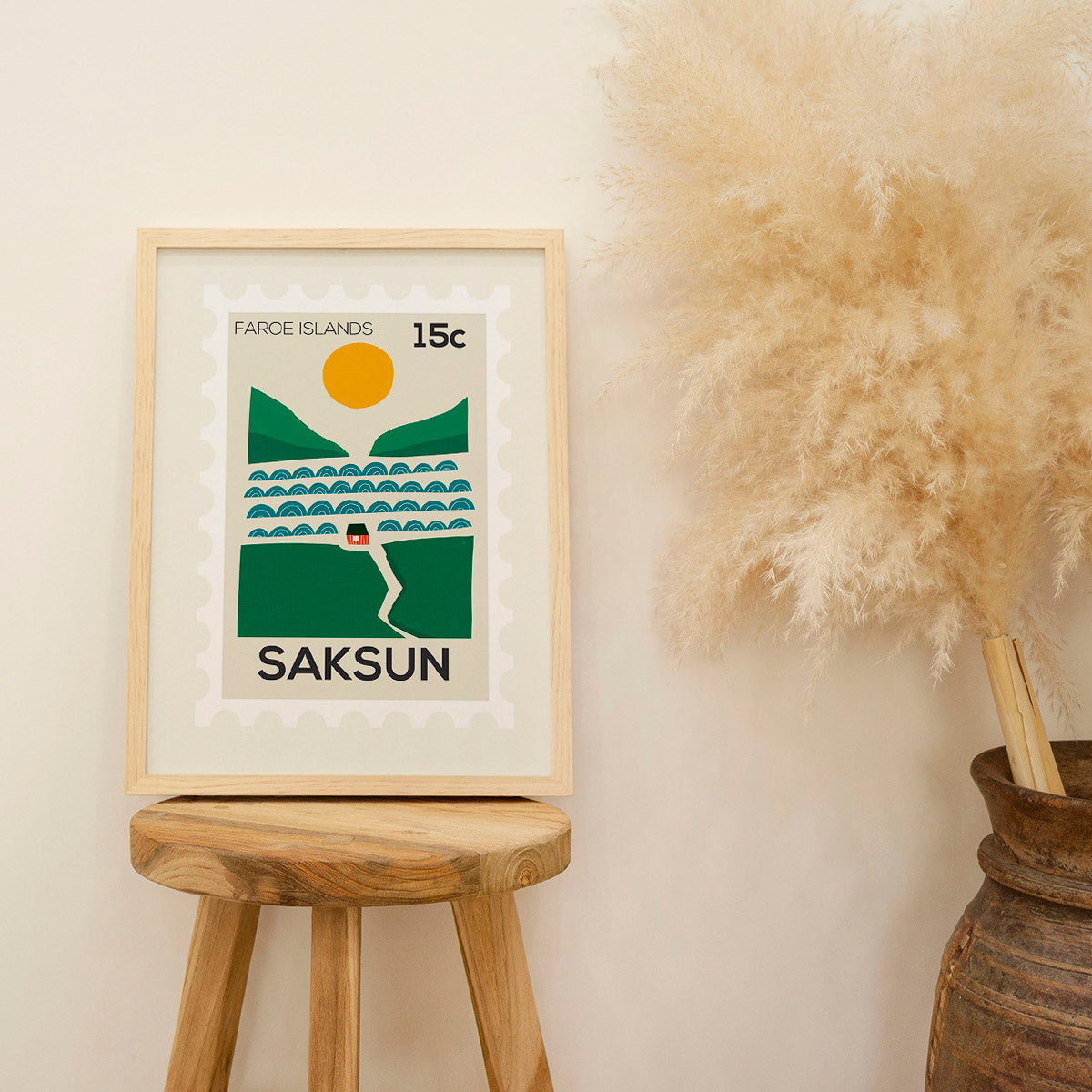 Framed artwork with 'Saksun' design on a wooden stool against a beige wall.