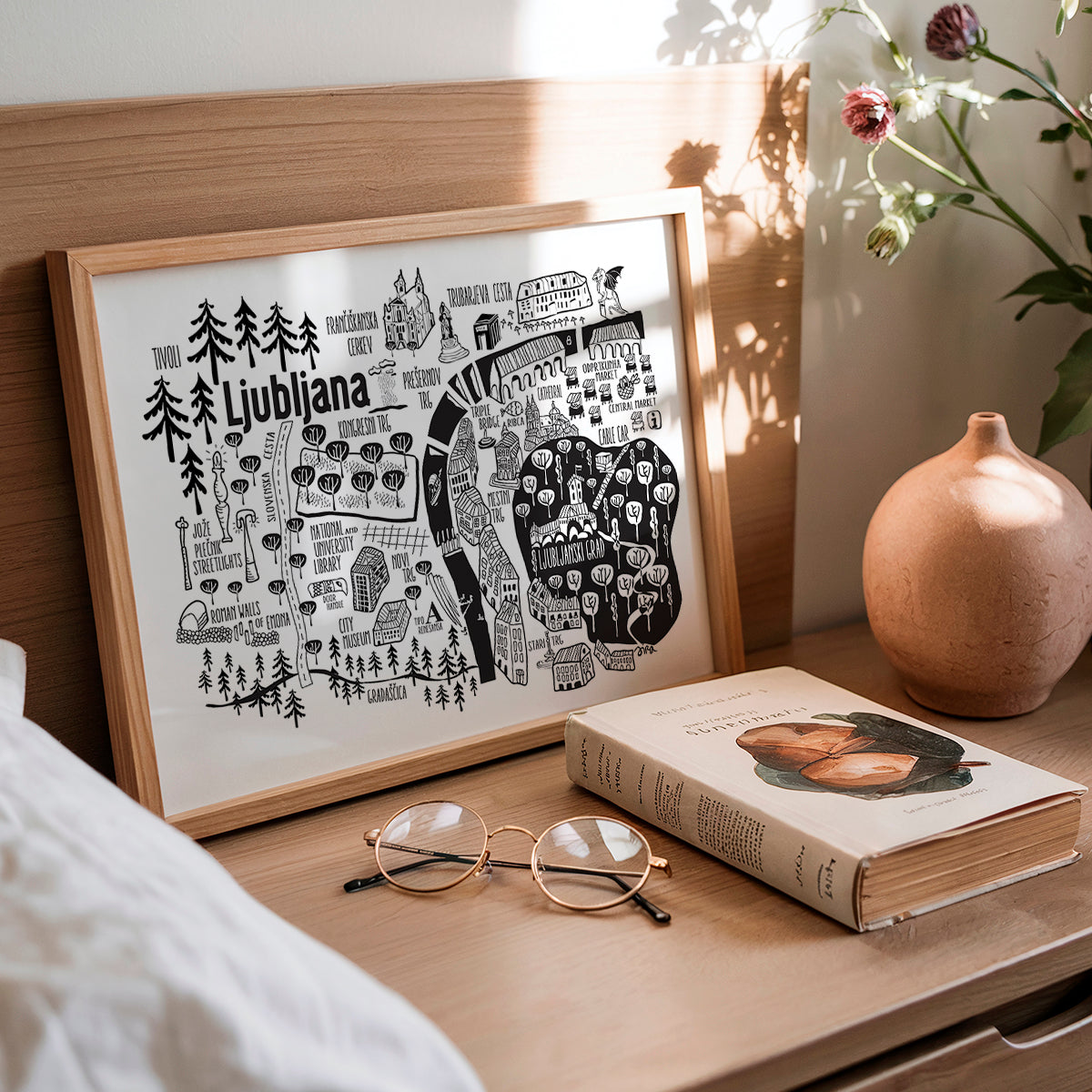 Framed map of Ljubljana on a wooden surface with a book and glasses.