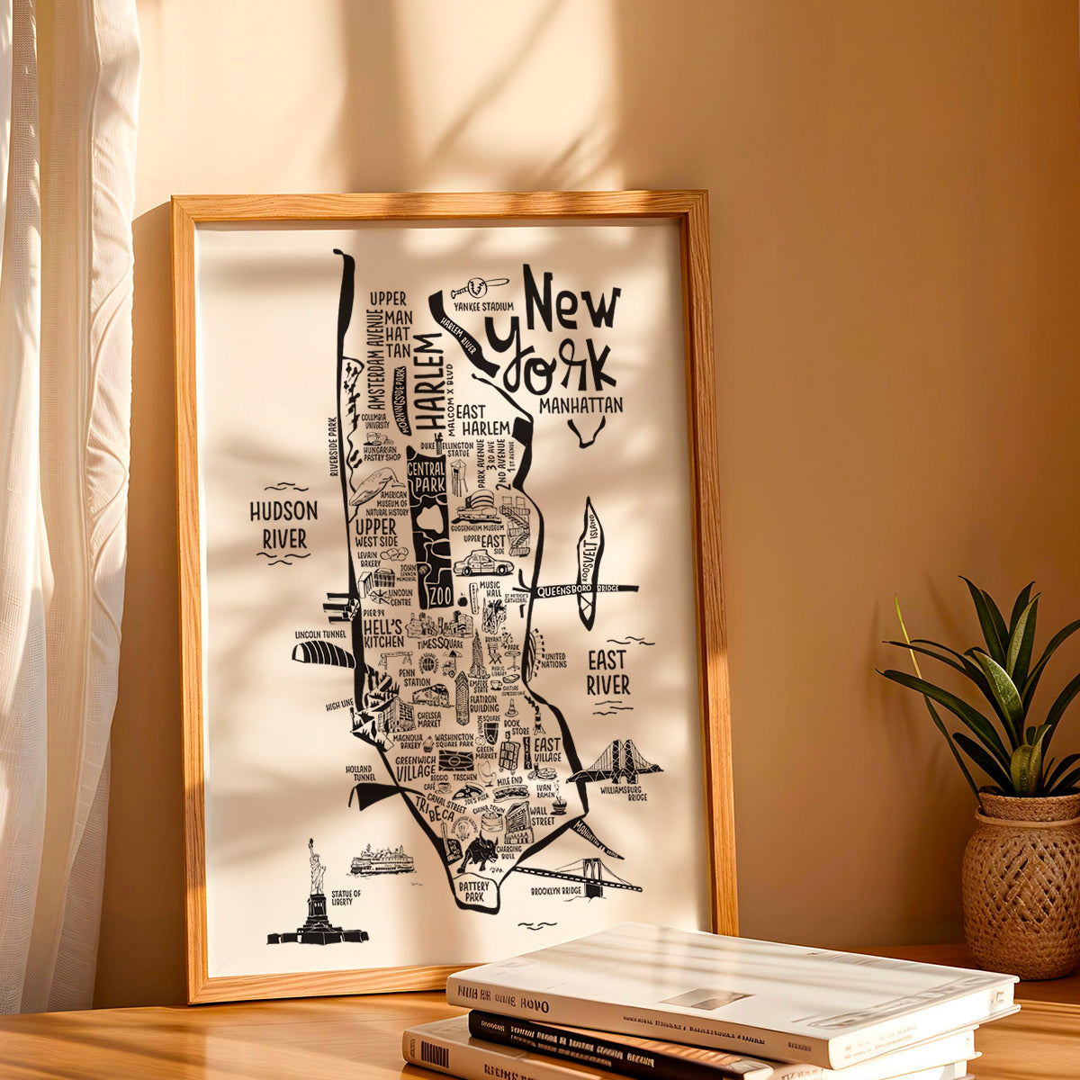 Framed map of New York City on a wall with a plant and books below