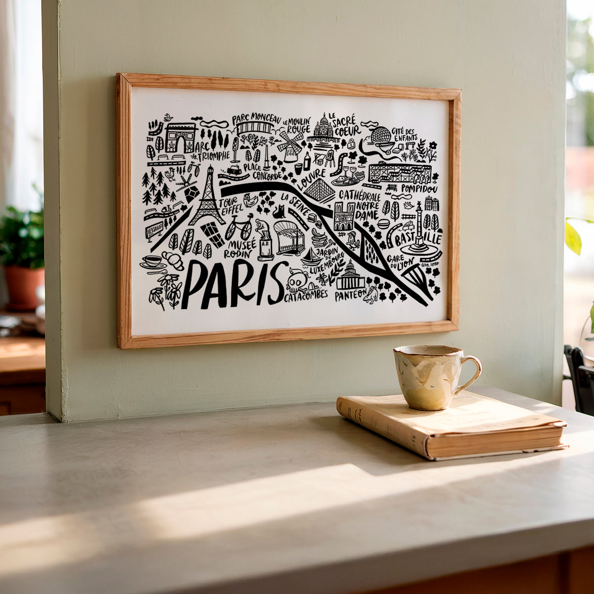 Framed map of Paris on a wall with a cup and book on a table below.
