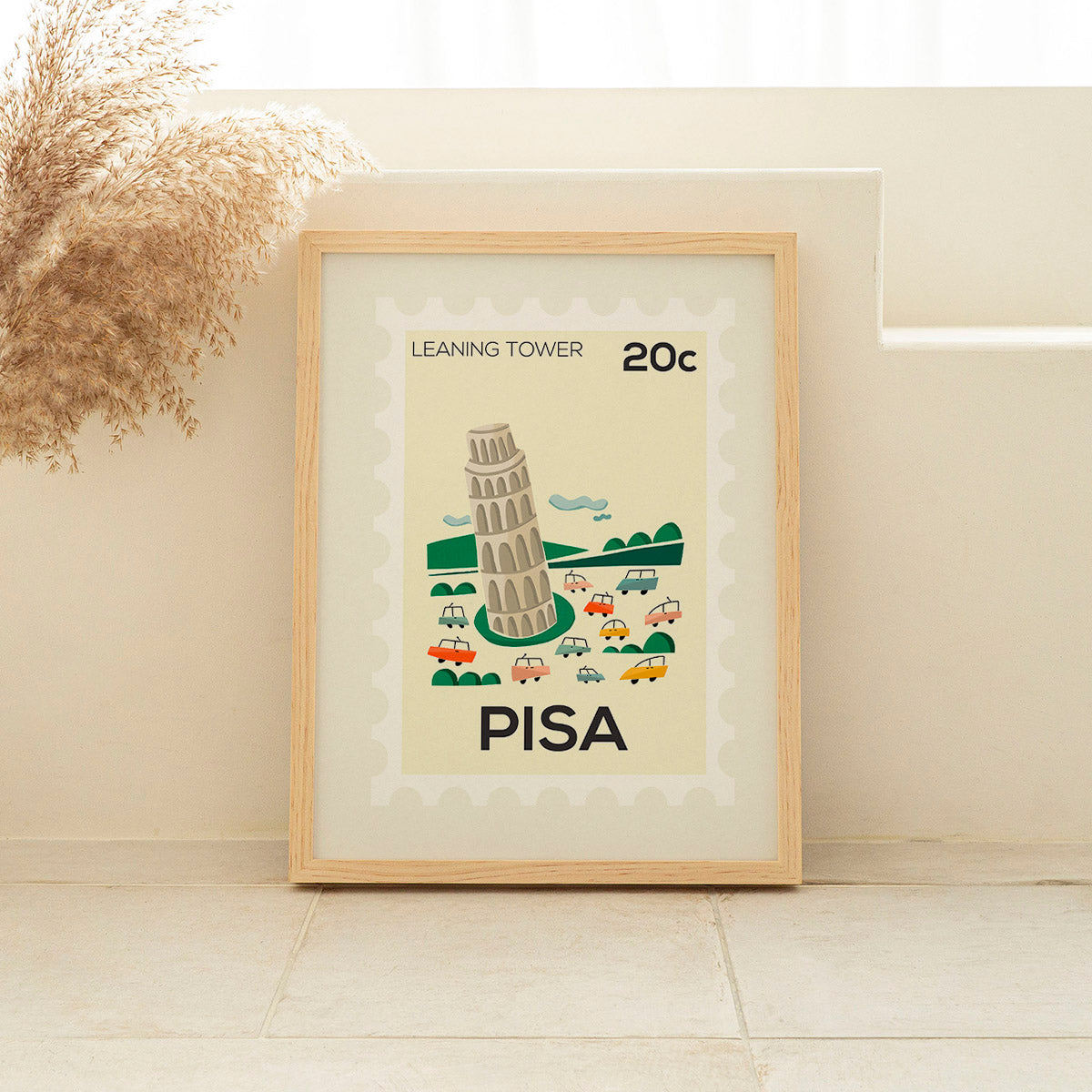 Framed poster of the Leaning Tower of Pisa with cars around it, on a light wall.