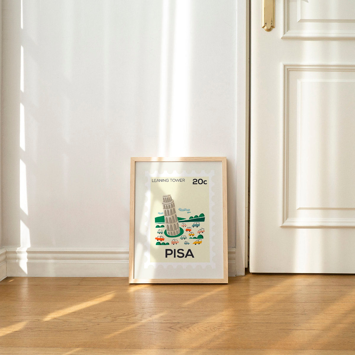 Framed artwork of the Leaning Tower of Pisa on a wooden floor with white walls.