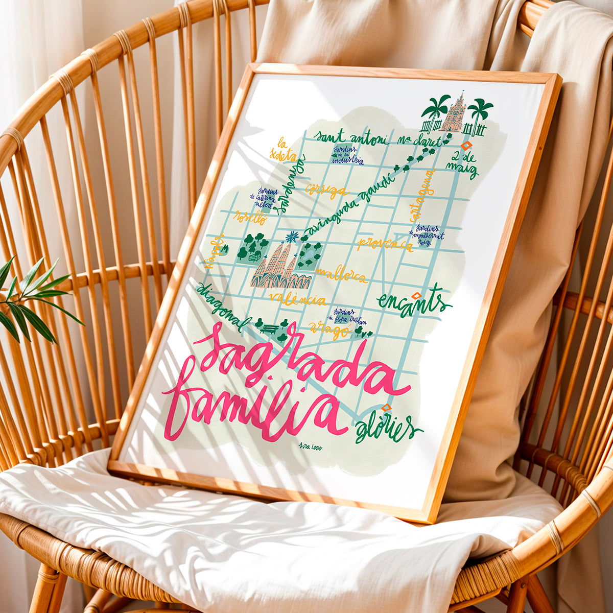 Framed map of Sagrada Familia in BArcelona on a wicker chair with a beige cushion.
