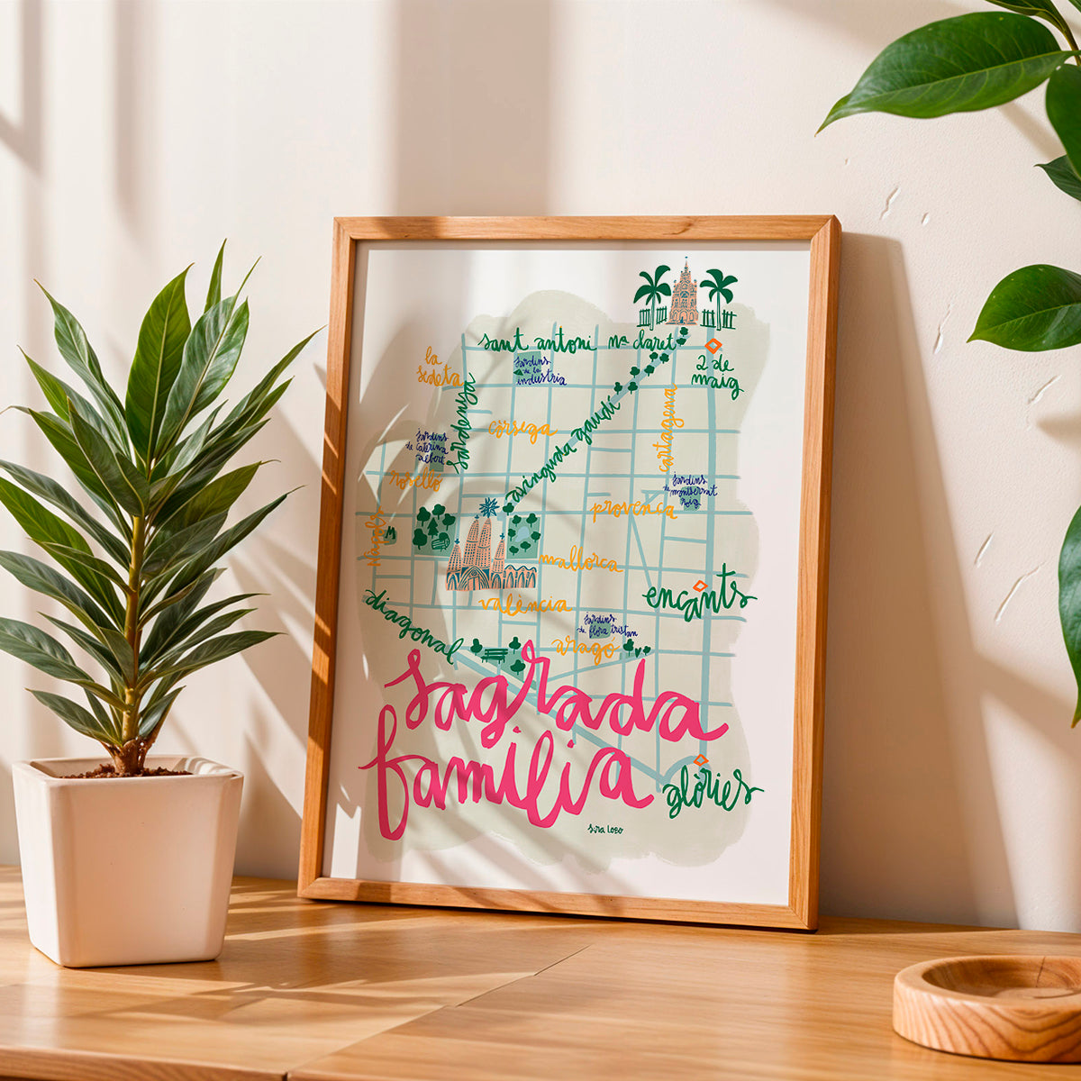 Framed map art piece of Sagrada Familia in BArcelona on a wooden surface with plants in the background