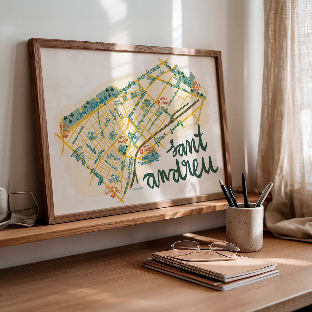 Framed map of Sant Andreu on a wooden shelf with stationery items.