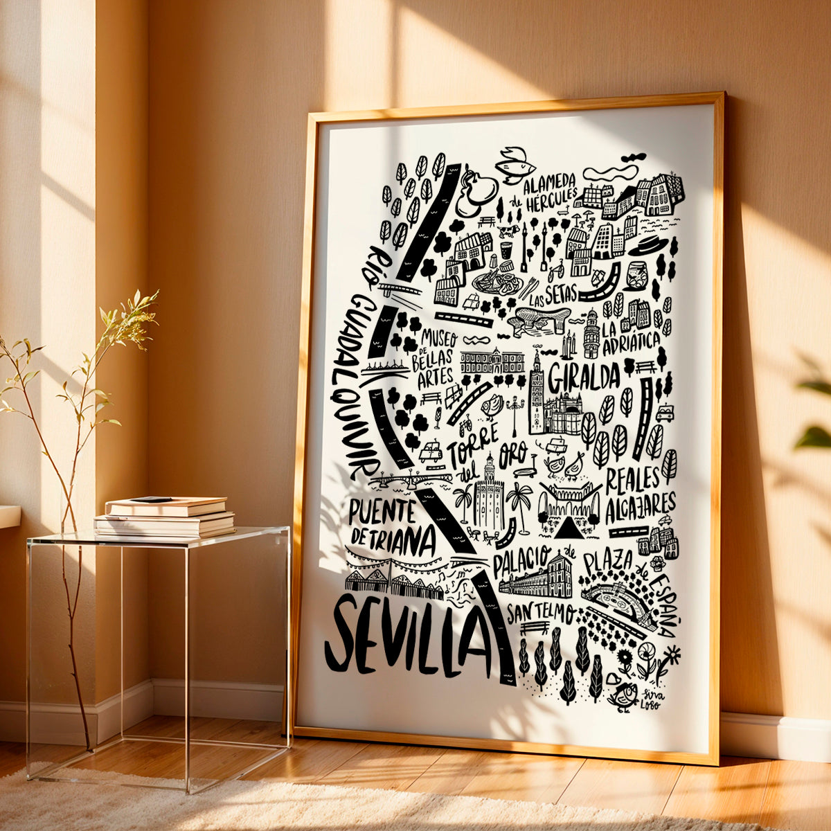 Framed artwork of a map of Sevilla with black illustrations on a white background, placed on a wooden floor.