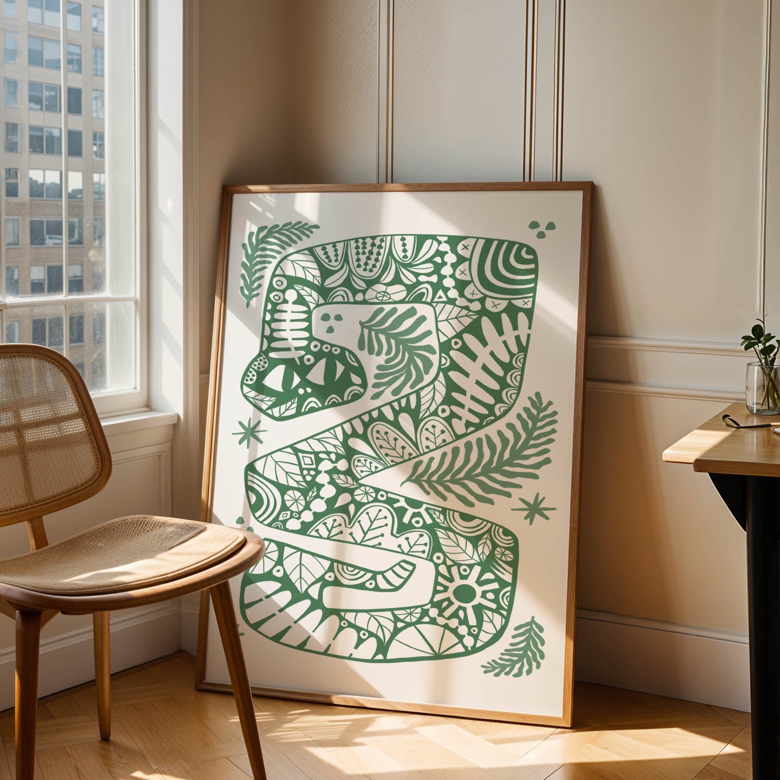 Framed green and white abstract artwork leaning against a wall in a room with a chair and table.