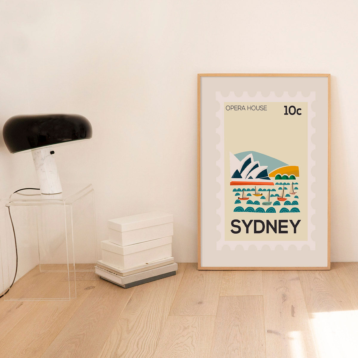 Framed artwork of the Sydney Opera House on a wall in a room with a lamp and books.