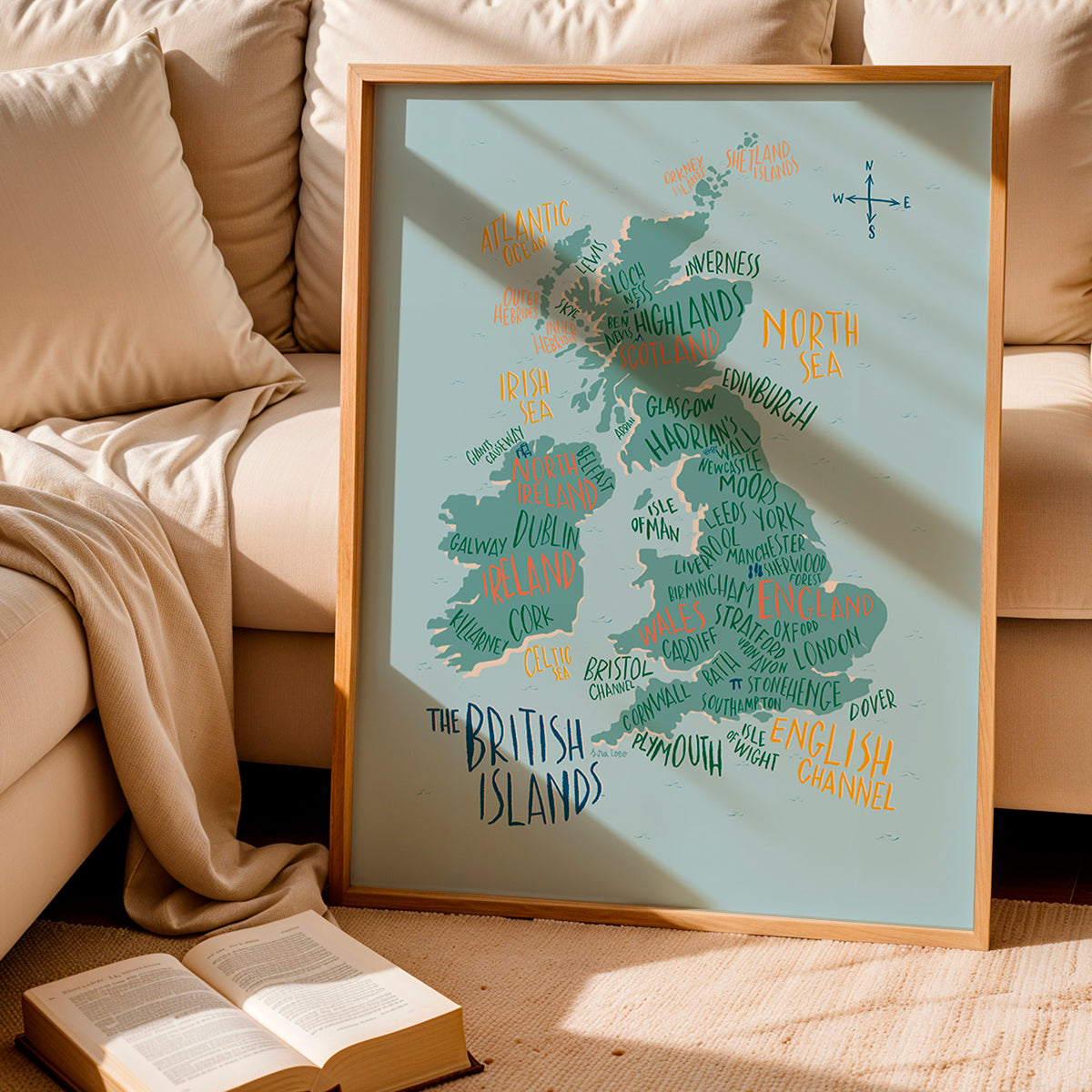 Framed map of the British Isles on a beige couch with an open book.