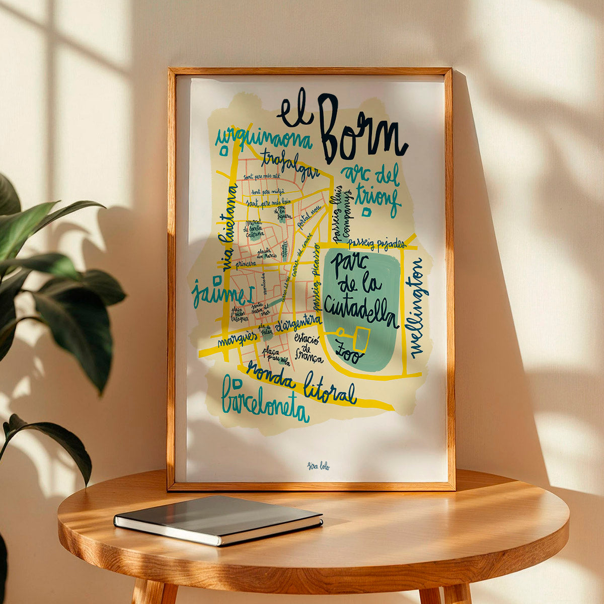 Framed map print of El Born district in Barcelona on a wooden table with a plant in the background.