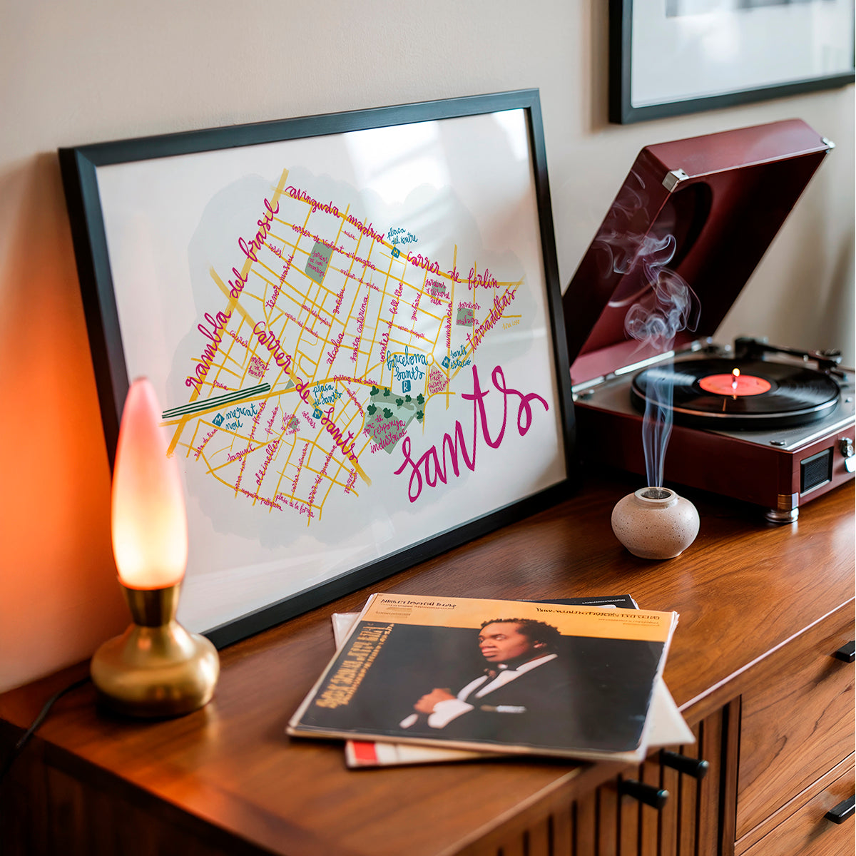 Framed map of Sants in Barcelona on a wooden surface with a record player and lit candle.