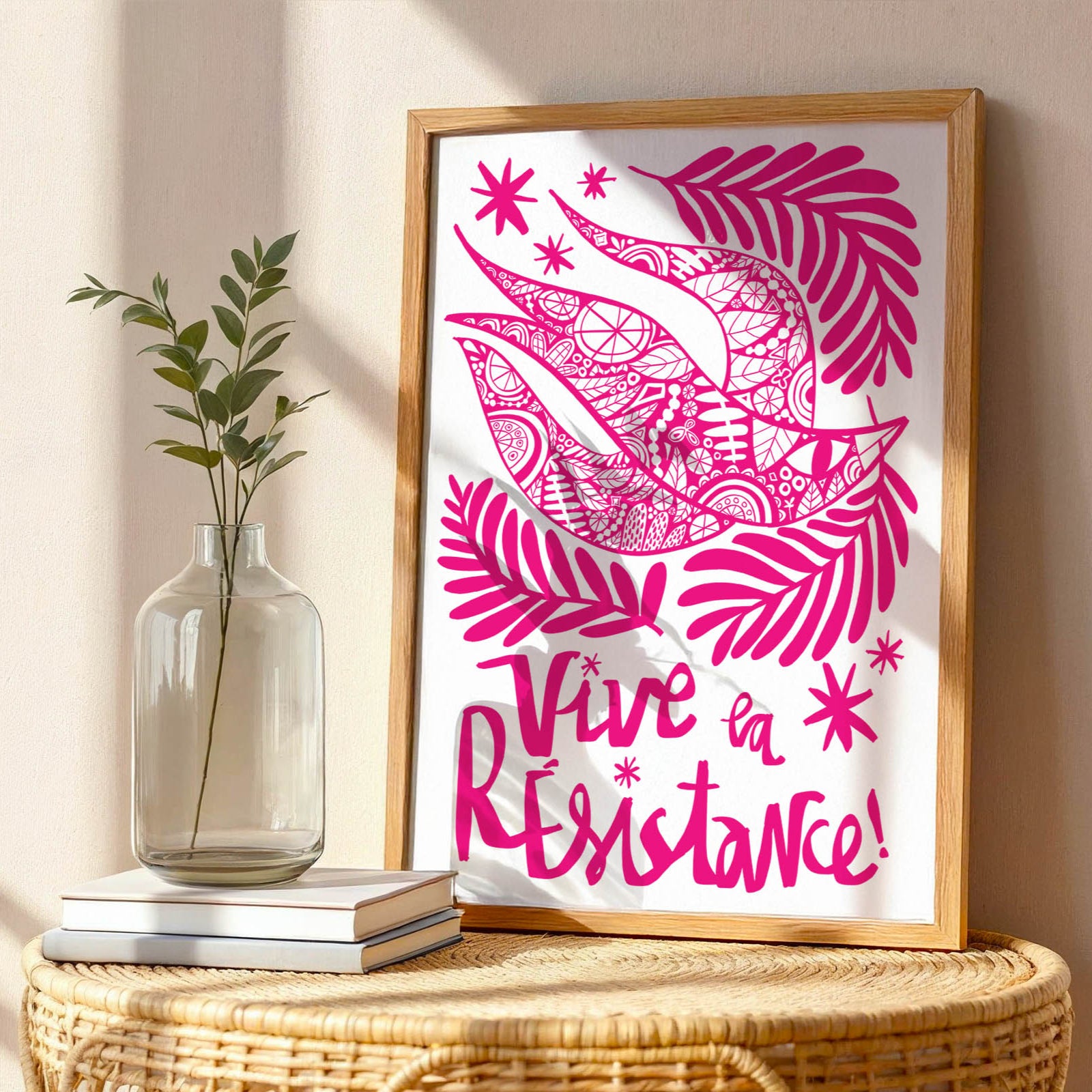 Framed artwork with pink design and text on a table with a vase and books.