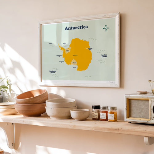 Framed map of Antarctica on a wall above a wooden shelf with kitchen items.