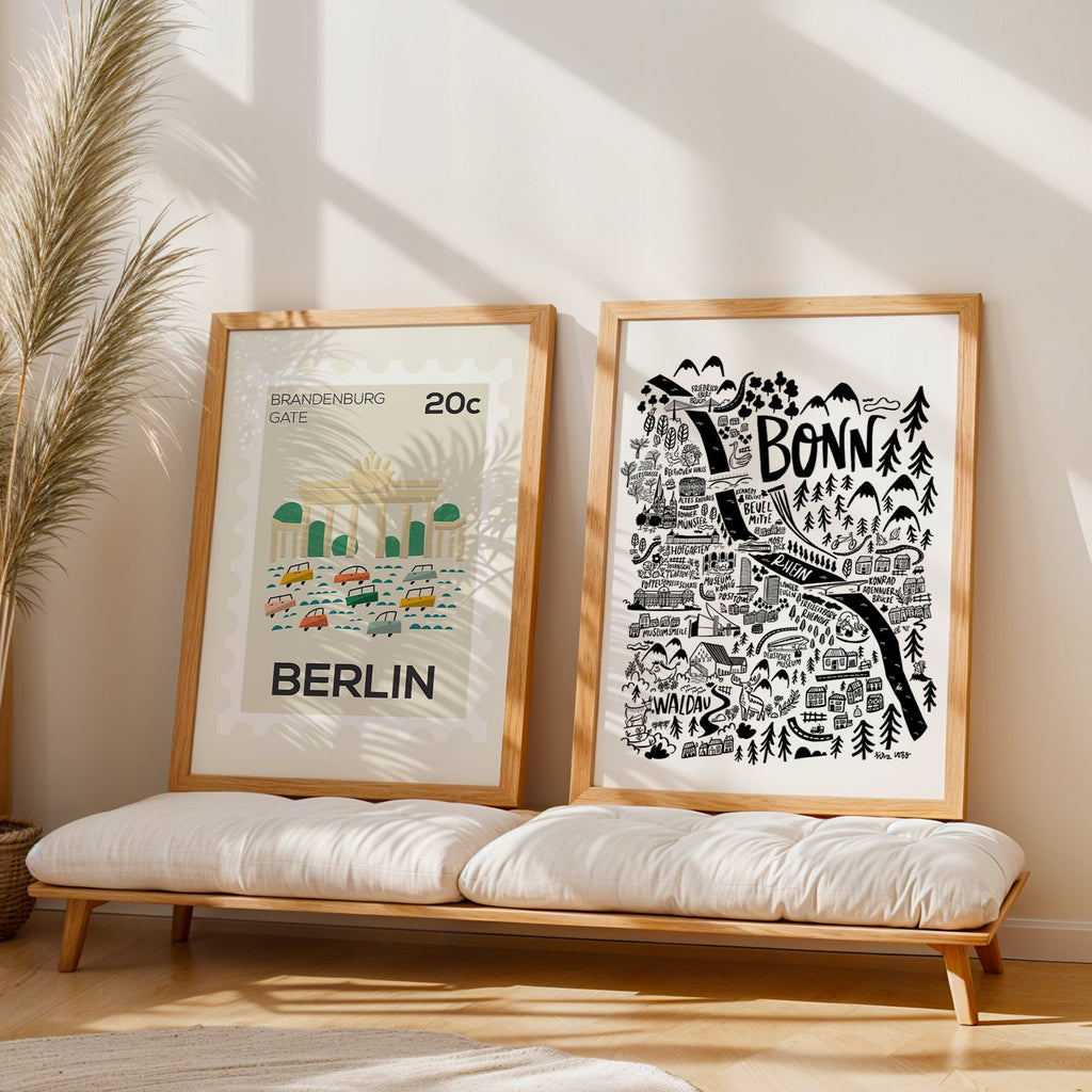 Two framed prints of Berlin and Bonn on a wooden bench with a plant in the background.