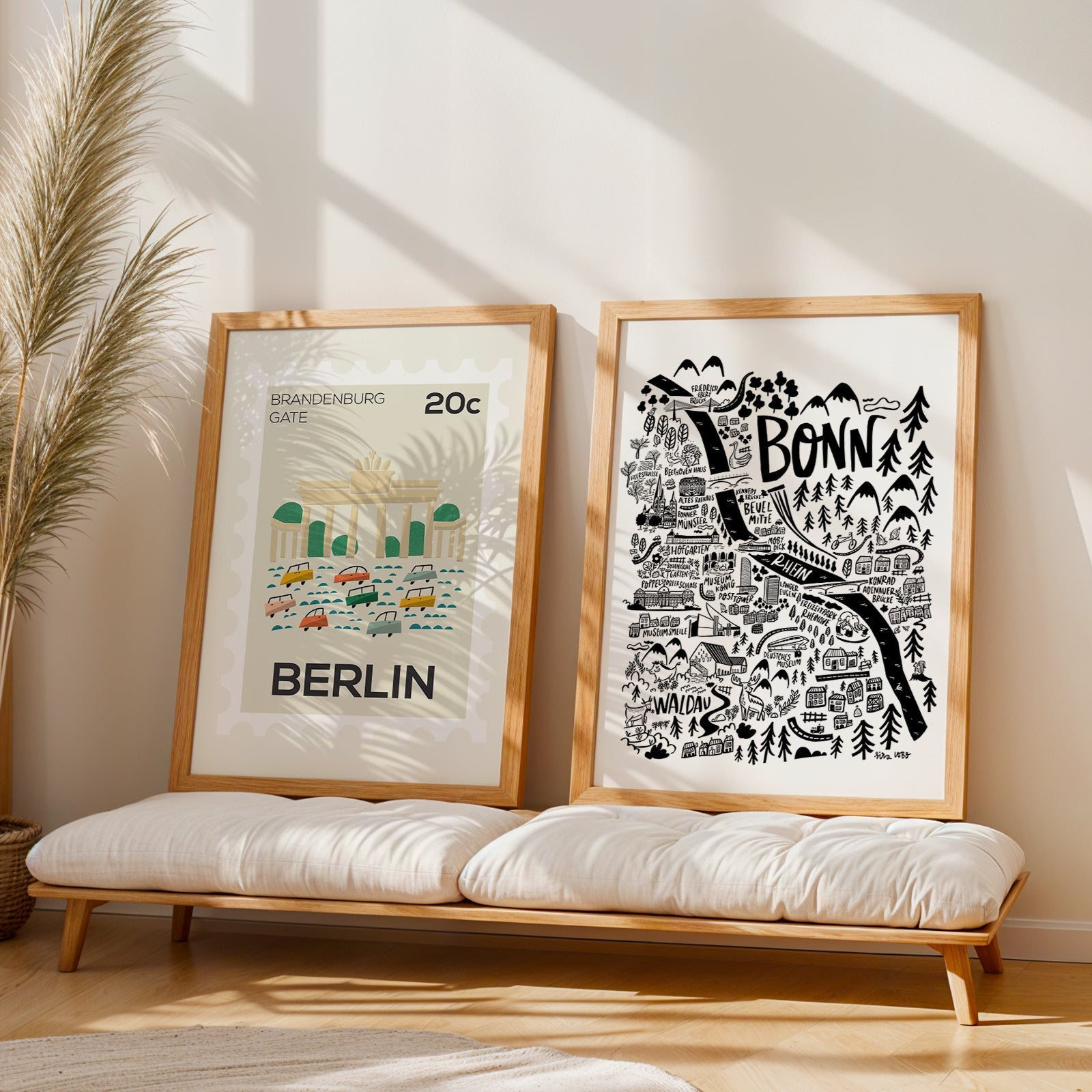 Two framed prints of Berlin and Bonn on a wooden bench with a plant in the background.