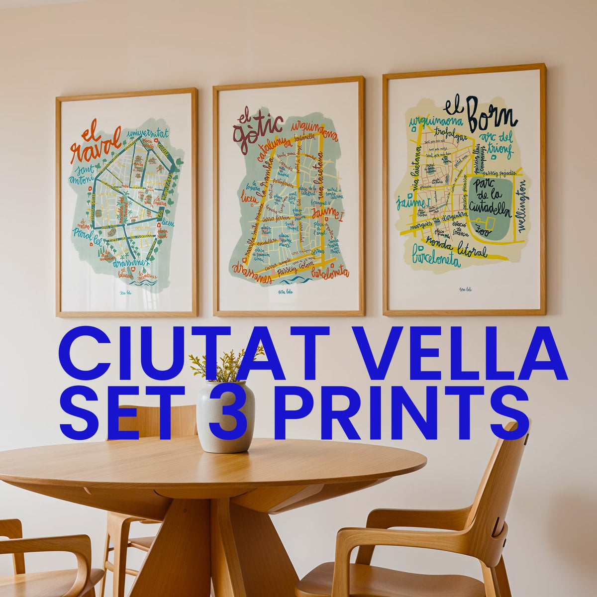 Three framed artworks on a wall above a wooden table with chairs.