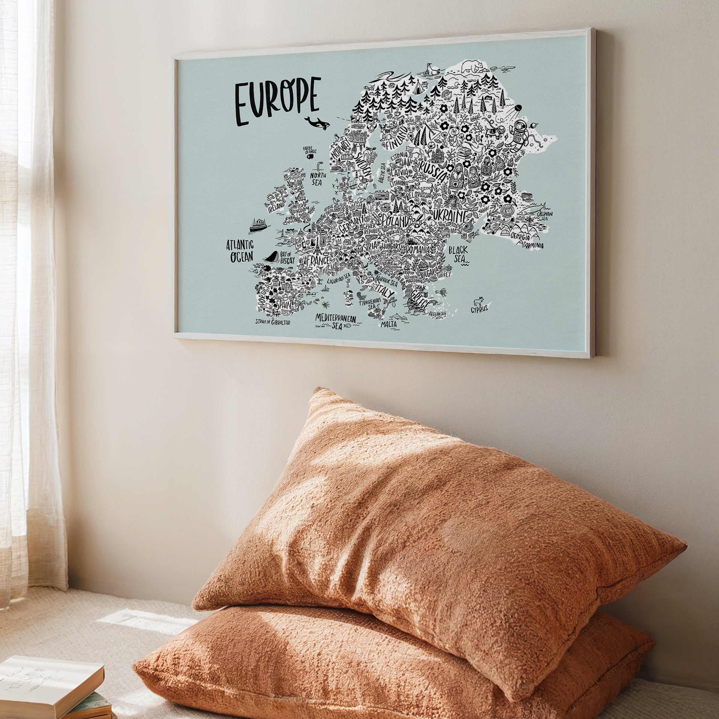 Framed map of Europe on a wall above two pillows on a floor.