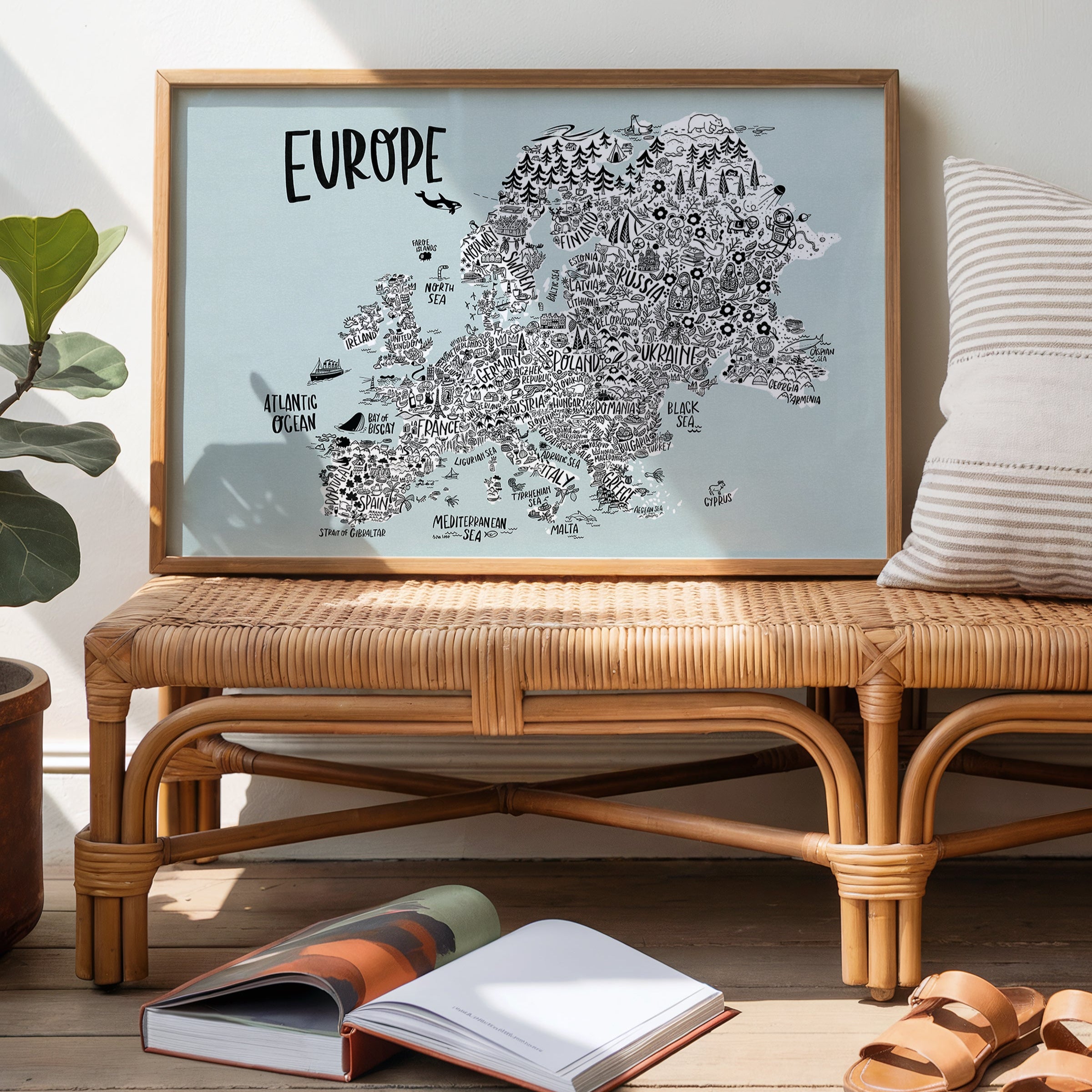 Framed map of Europe on a wooden bench with books and sandals in the foreground.