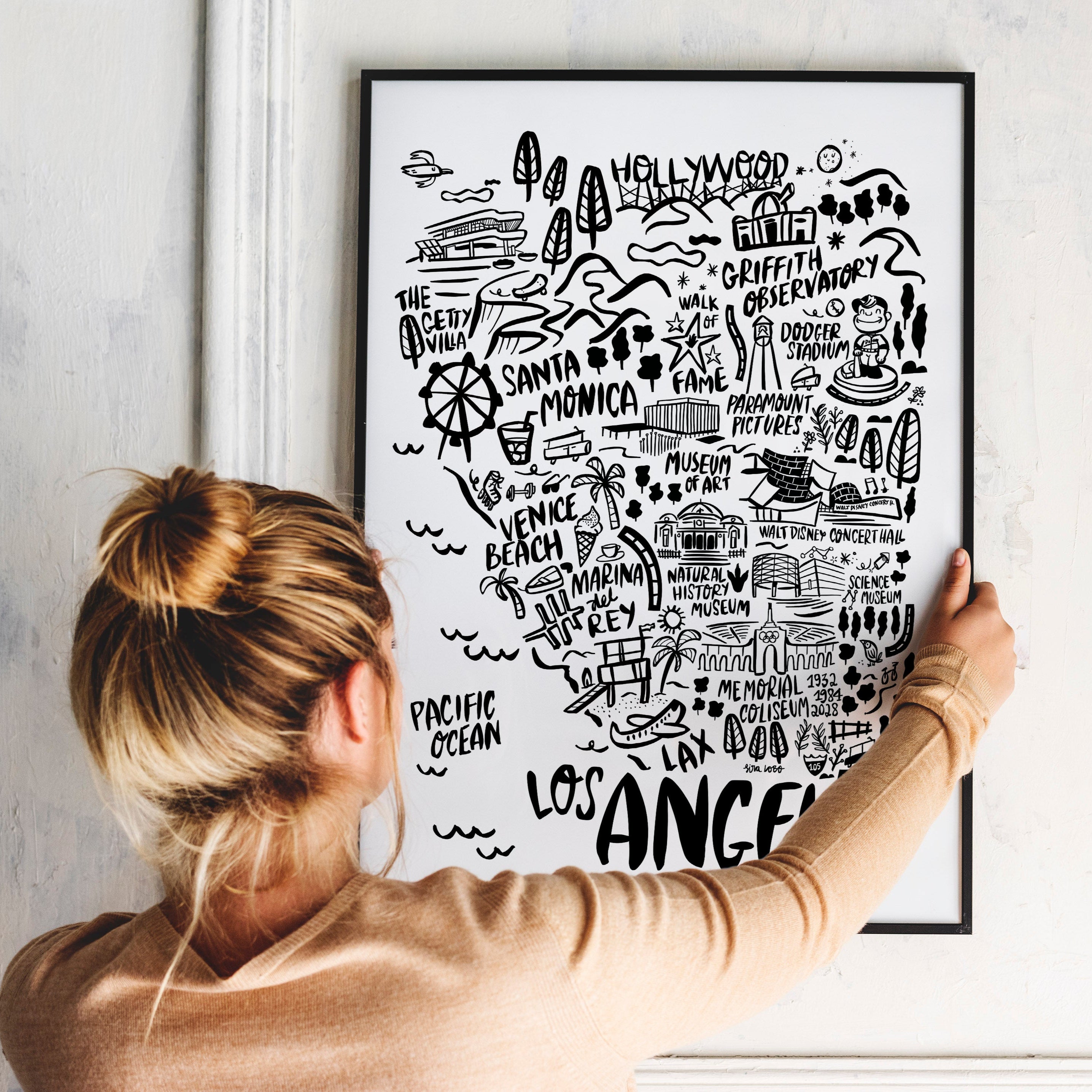 Person holding a framed map of Los Angeles against a white wall