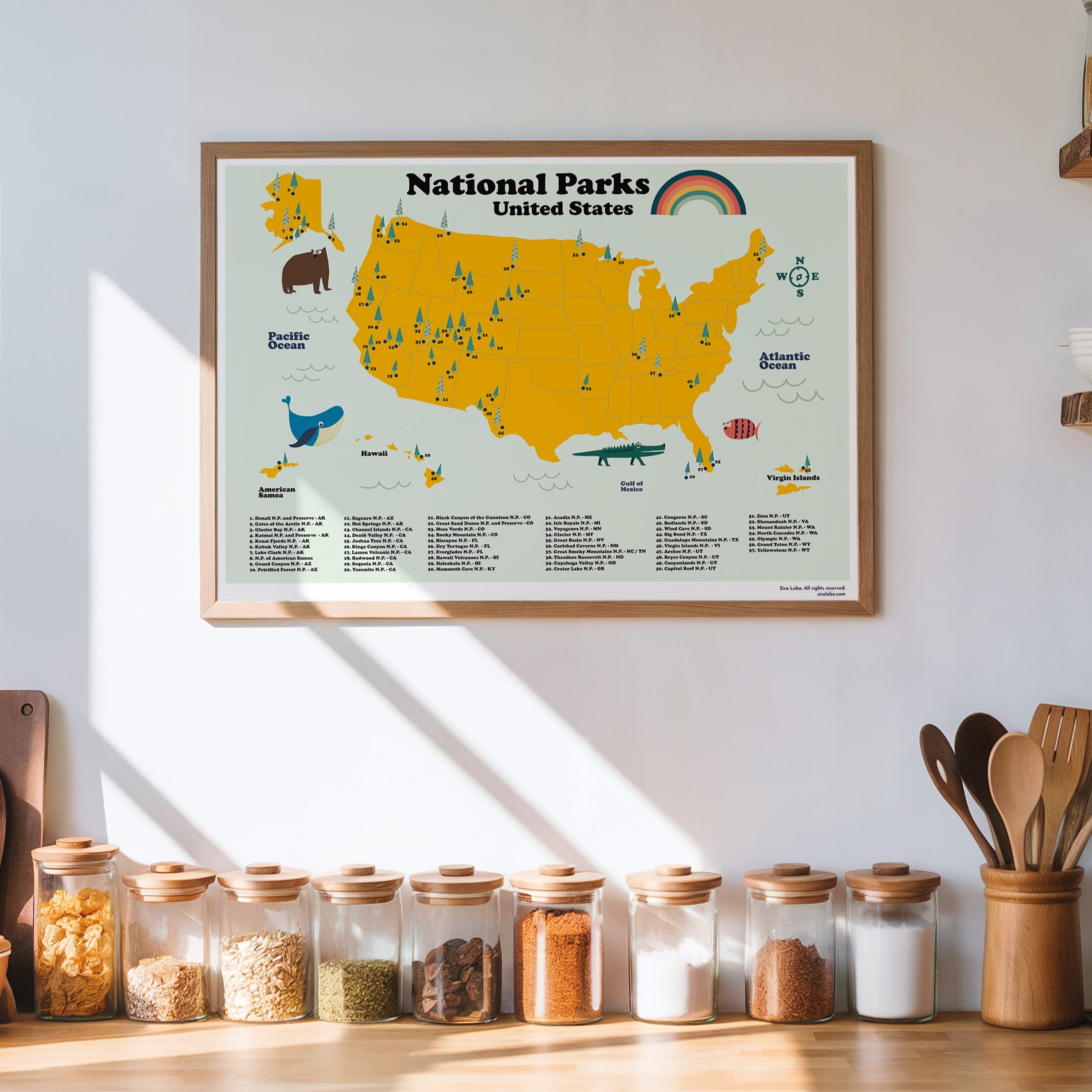 Framed map of National Parks United States on a wall above a wooden shelf with jars and kitchen utensils.
