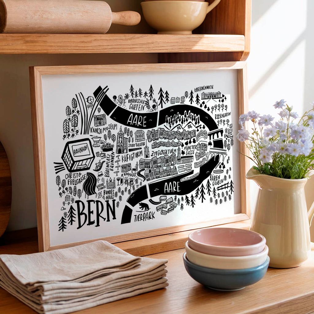 Framed map print on a kitchen counter with bowls, flowers, and a towel.