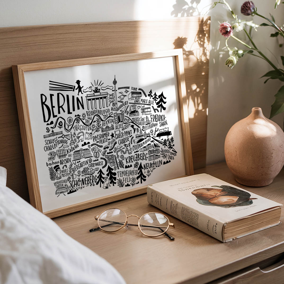 Framed artwork with 'Berlin' design, book, and glasses on a wooden surface.