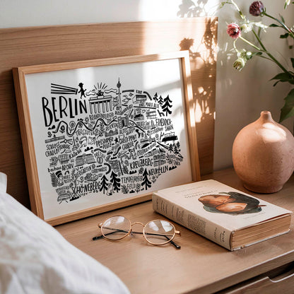 Framed artwork with 'Berlin' design, book, and glasses on a wooden surface.