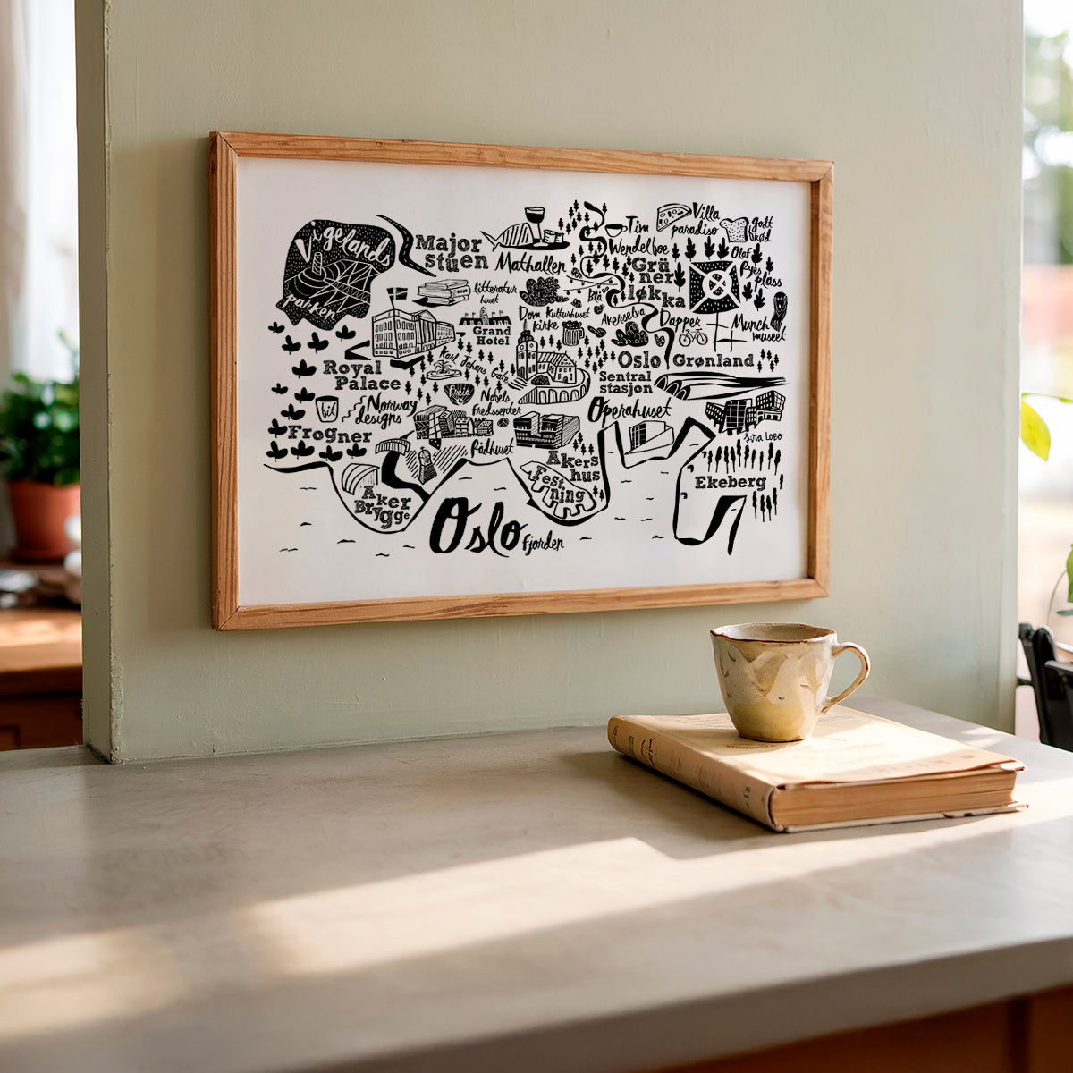 Framed map of Oslo on a wall with a cup and book on a surface below.