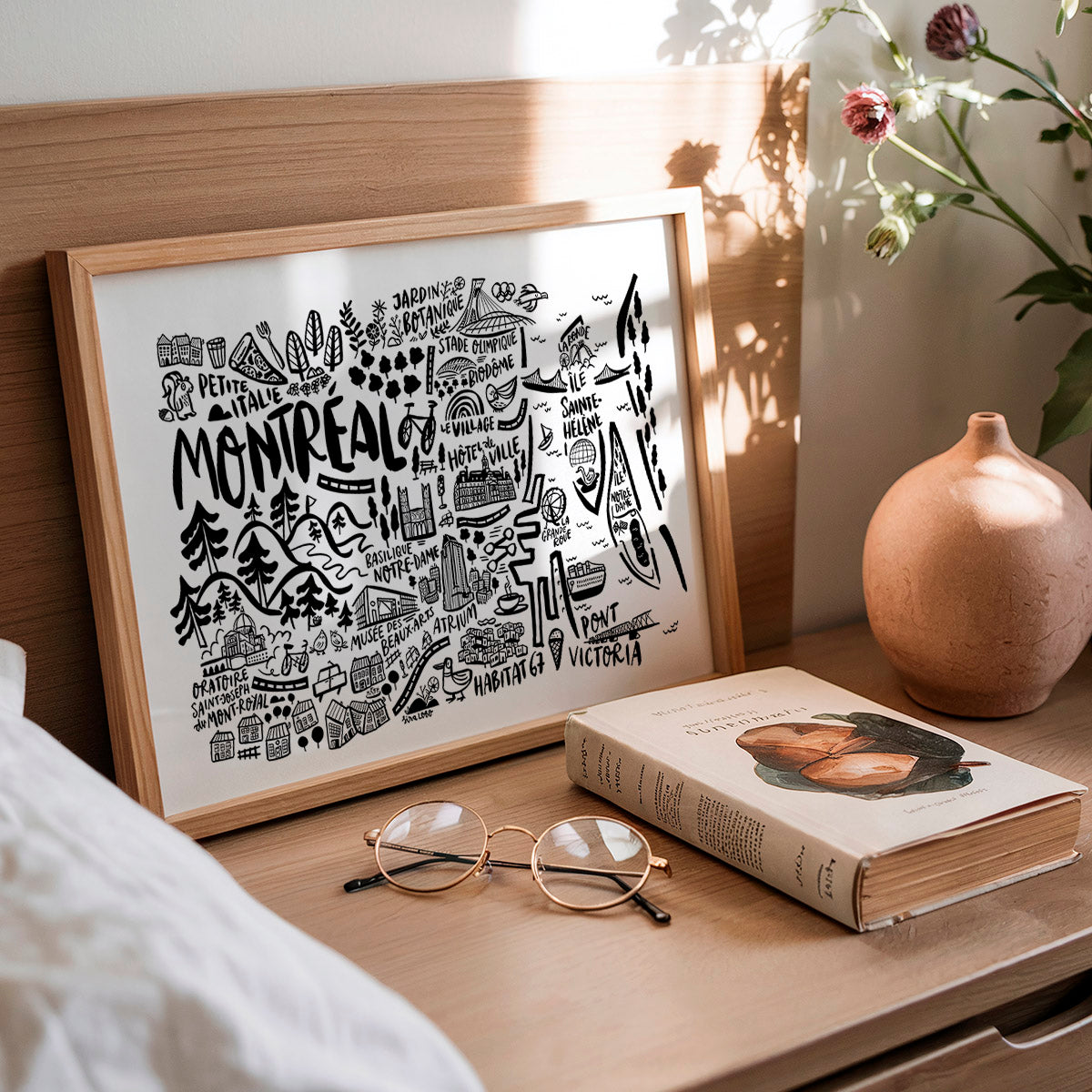 Framed map of Montreal on a wooden surface with a book and glasses.