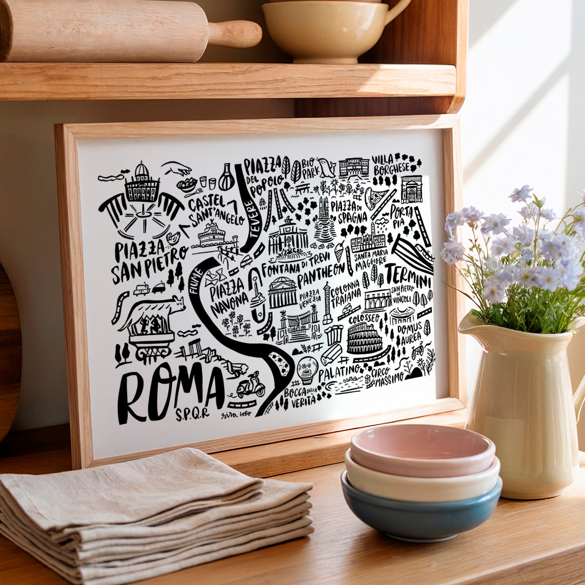 Framed artwork with 'Roma' design on a kitchen counter with bowls and flowers.