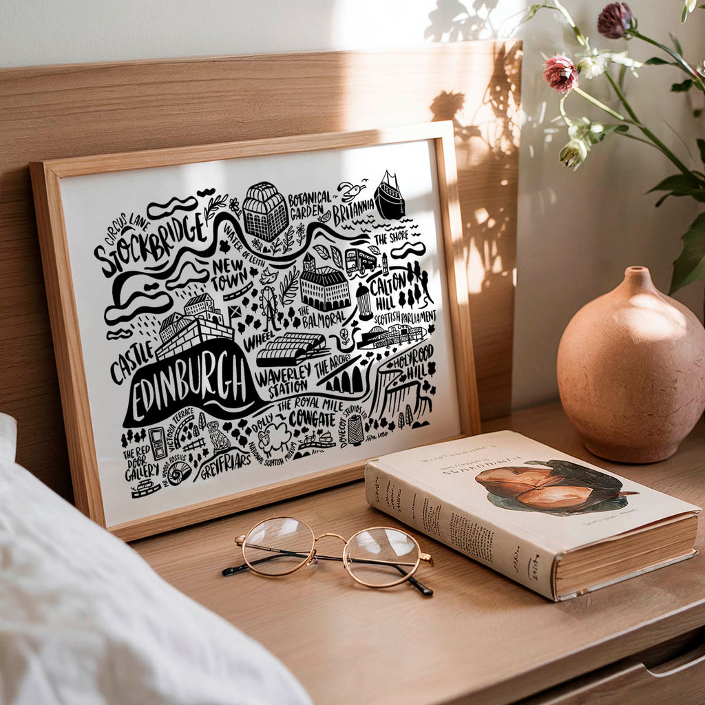 Framed map of Edinburgh on a wooden surface with a book and glasses.
