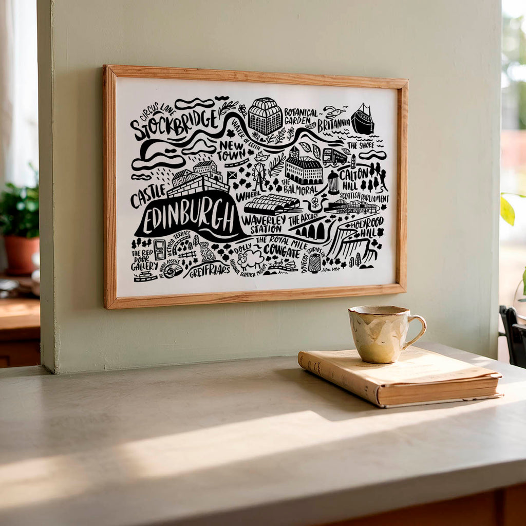 Framed map of Edinburgh on a wall with a cup and book on a table below.