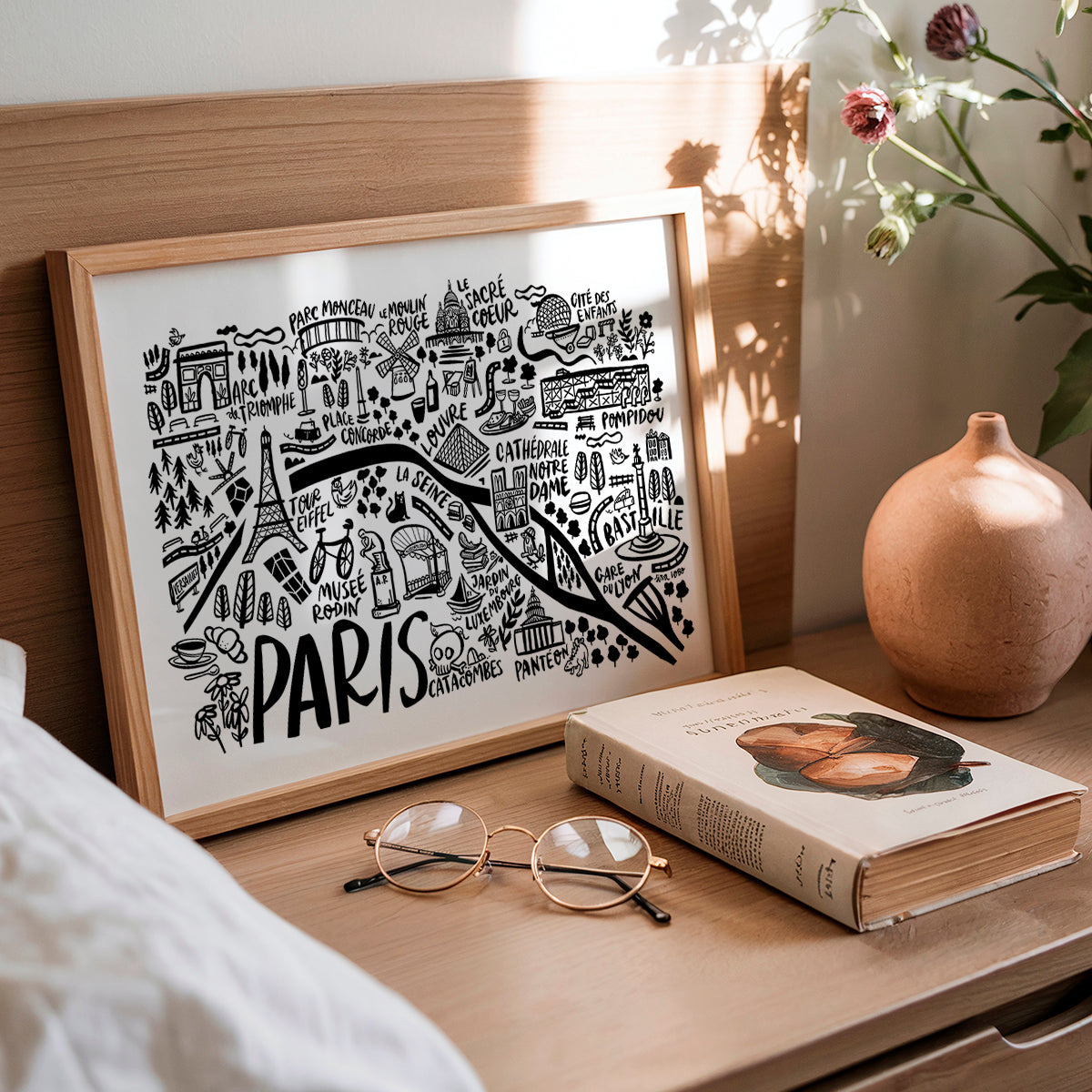 Framed map of Paris on a wooden surface with a book and glasses.