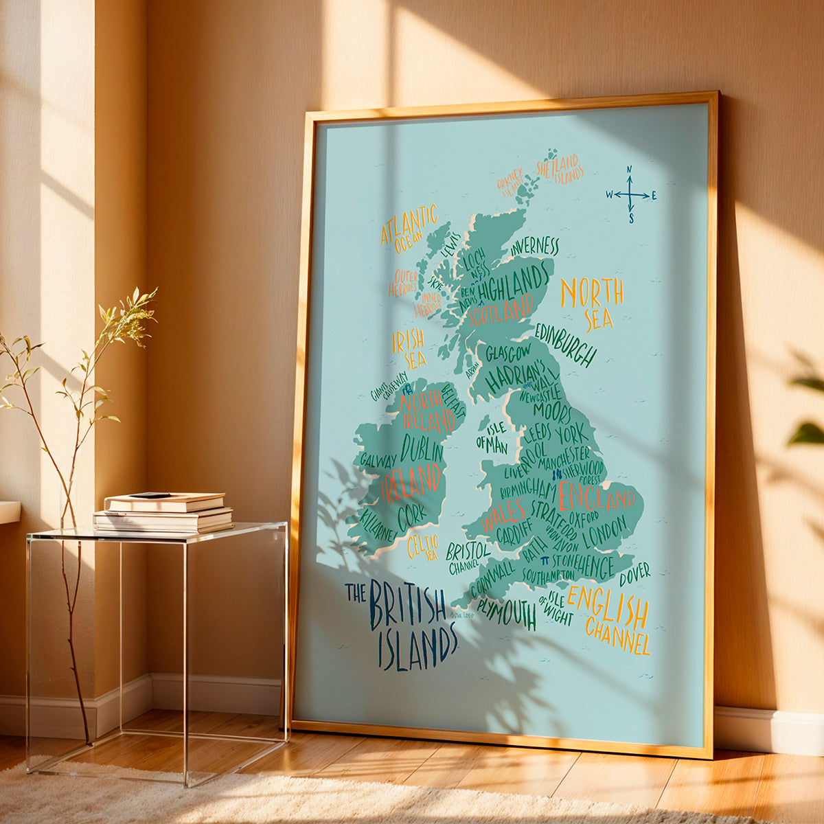 Framed map of the British Isles on a wall in a room with a side table and plant.