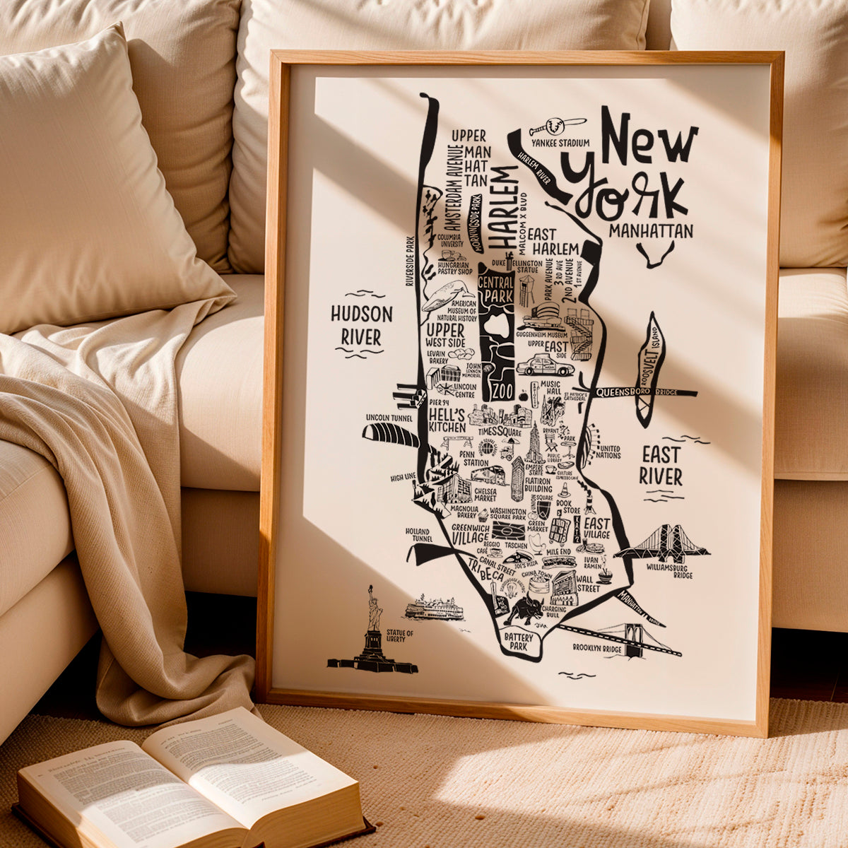 Framed map of New York City on a beige couch with an open book.