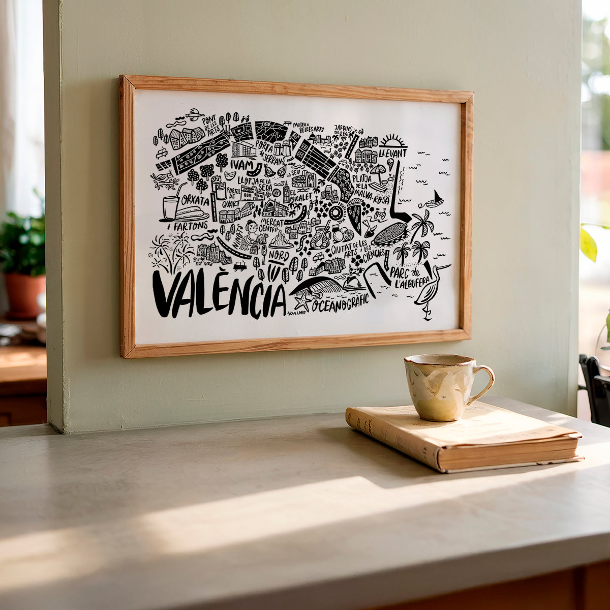 Framed map of Valencia on a wall with a cup and book on a surface below.